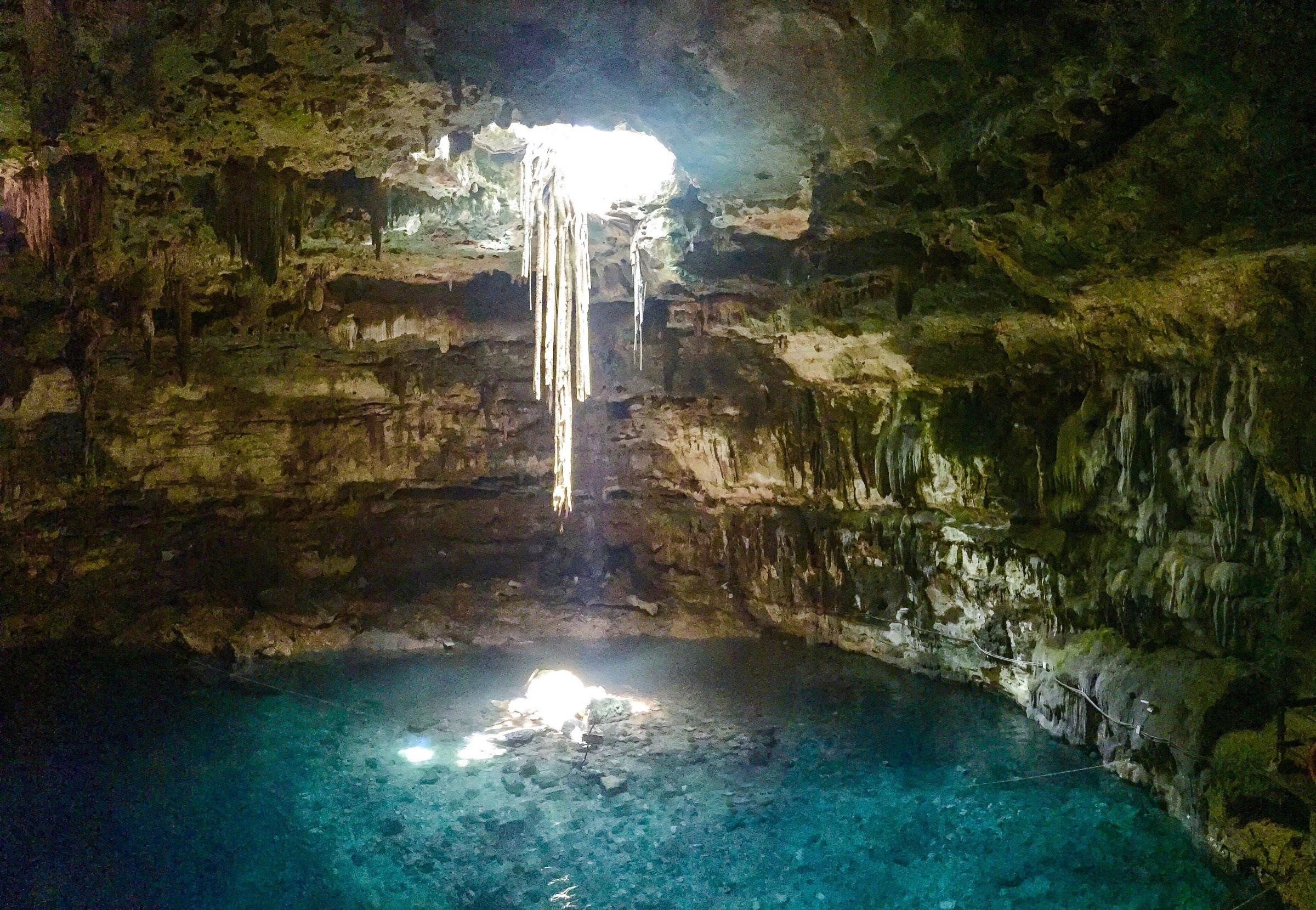 Cenote Samulá: un rayo de luz entra por la bóveda y cae sobre el agua turquesa, con raíces colgando
