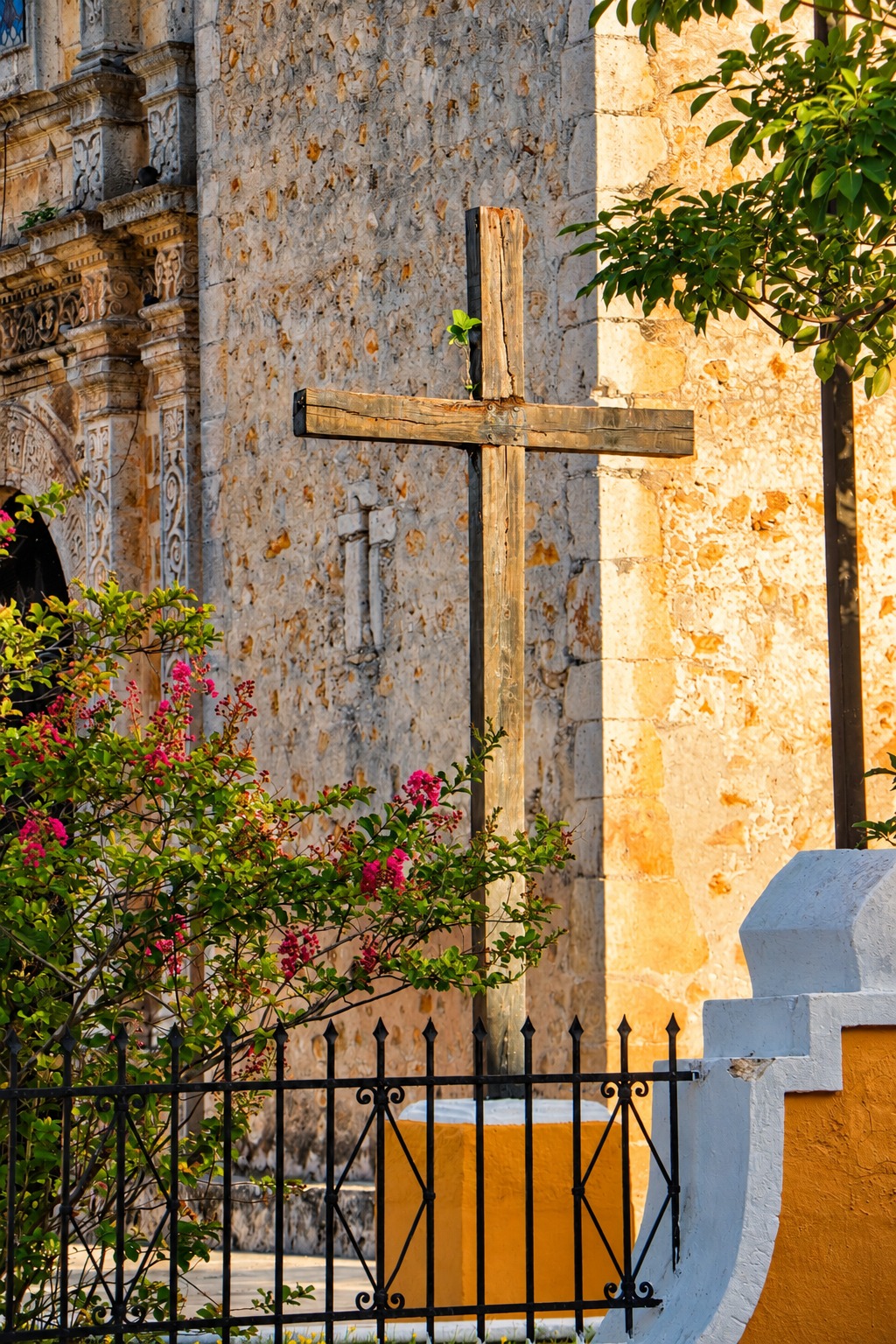 Cruz de madera en el atrio de una iglesia, con buganvilia al atardecer