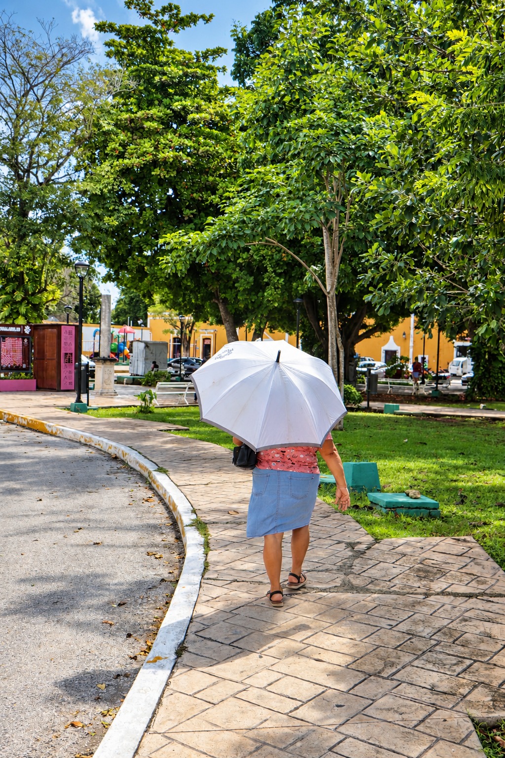 Mujer con sombrilla blanca caminando por un parque del centro